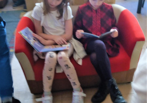Dwie uczennice siedzą na kanapie w sali bibliotecznej i czytają książki